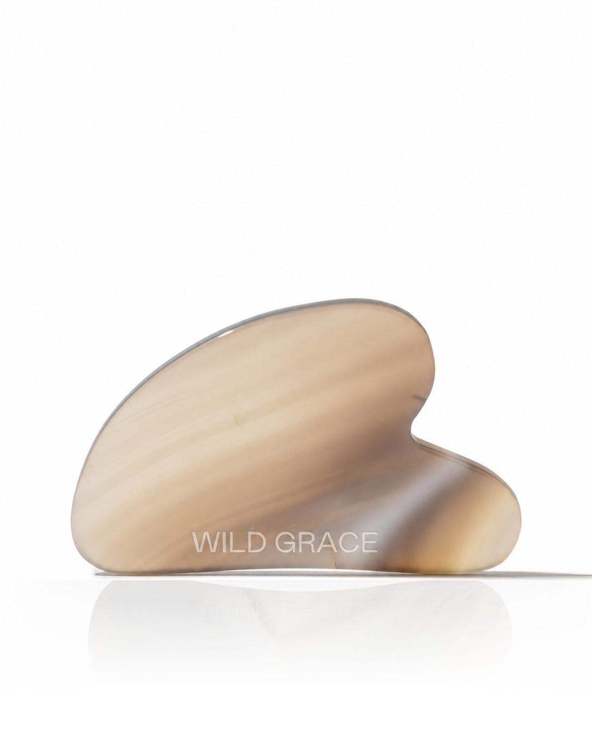 A curved, hand-shaped jade Gua sha massage tool with a translucent beige and light brown marbled pattern, resting on a reflective white surface against a white background. The brand name 'WILD GRACE' is subtly printed on the front.