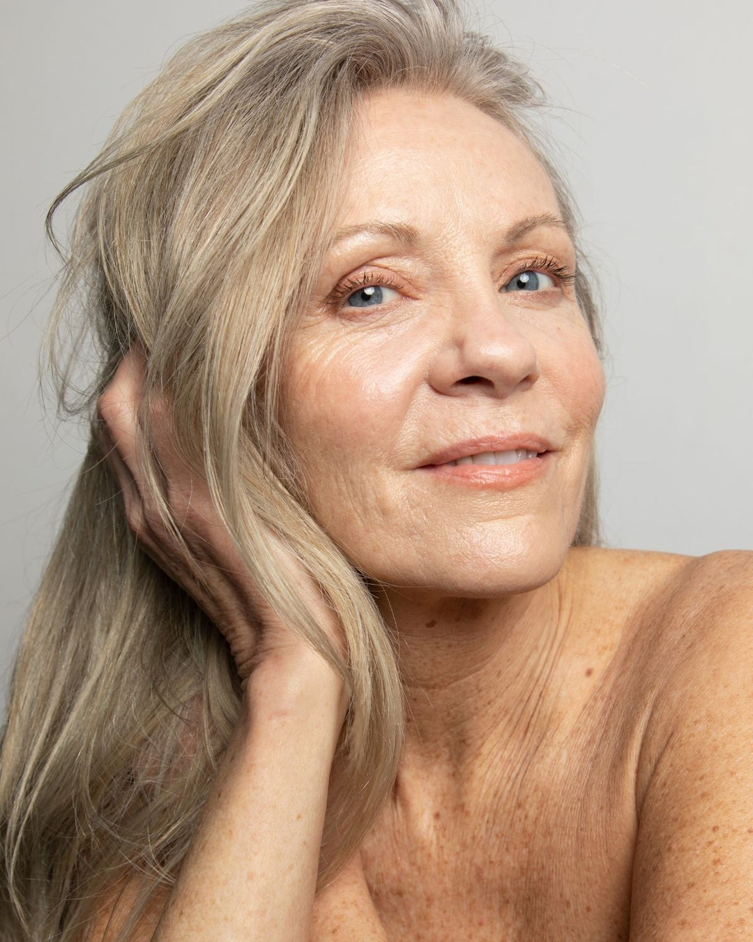 Woman with gray hair and visible skin texture on a plain background