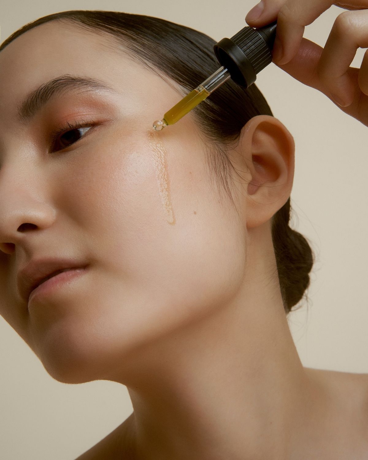 Woman applying a dropper of wild grace Elixir serum  to their face against a neutral background