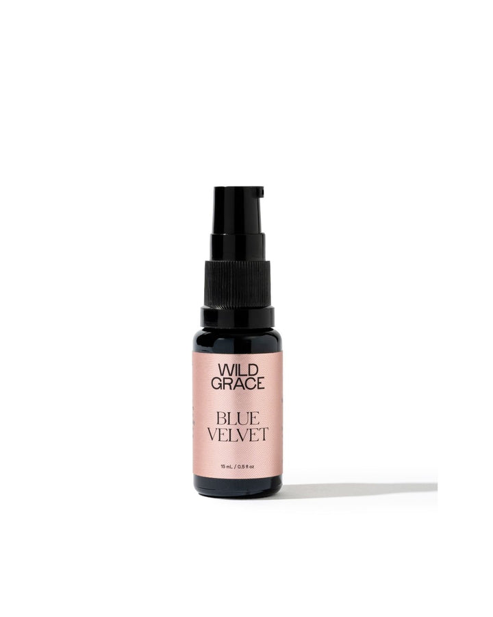 A small Wild Grace Blue Velvet spray bottle with a black pump and a dusty pink label, set against a plain white background with a soft shadow.