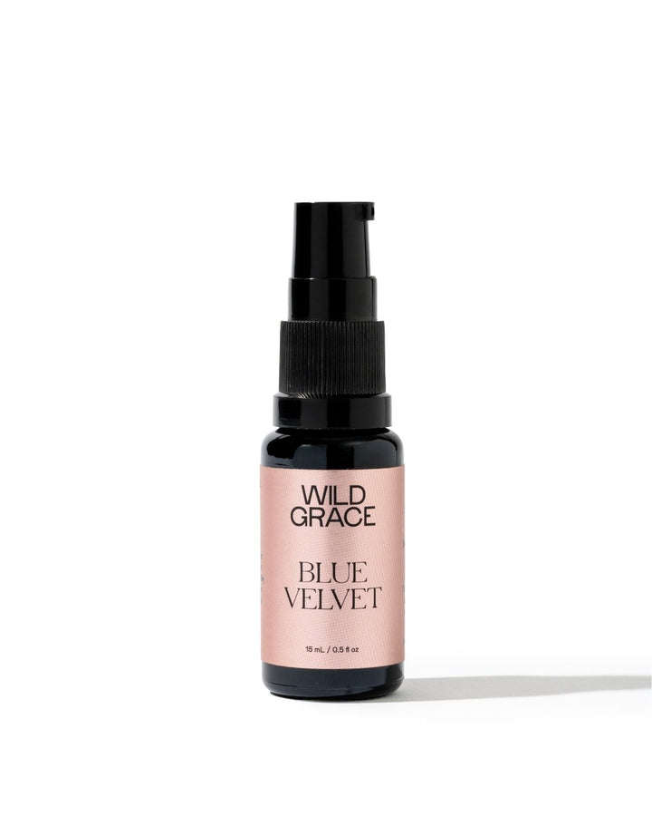 A small spray bottle of Wild Grace Blue Velvet hair product, featuring a black pump and a dusty pink label, set against a plain white background.