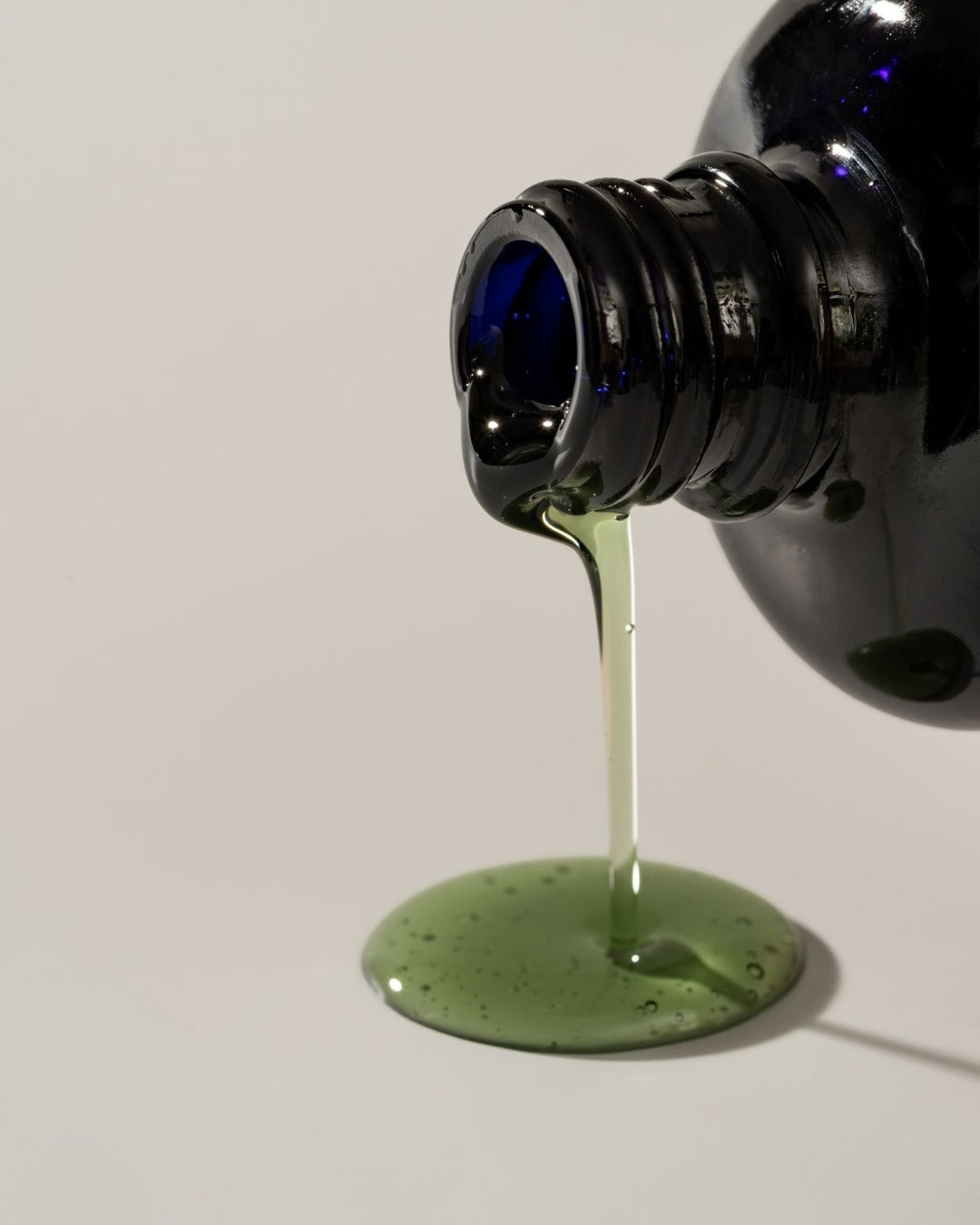 Green liquid being poured from a black bottle onto a white surface