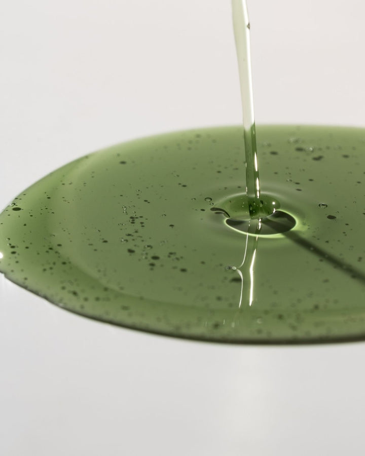 Green liquid being poured onto a green surface with a white background
