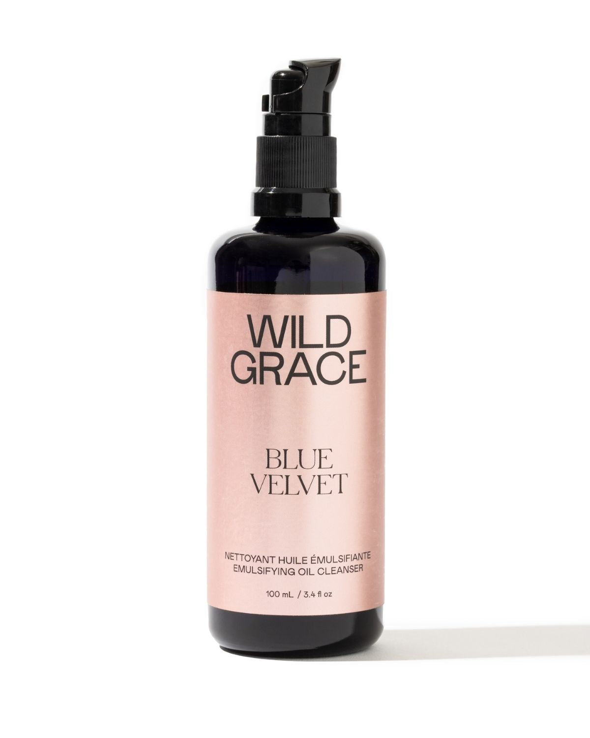 A 100 mL pump bottle of Wild Grace Blue Velvet Emulsifying Oil Cleanser, featuring a black bottle and a metallic pink label, set against a plain white background.