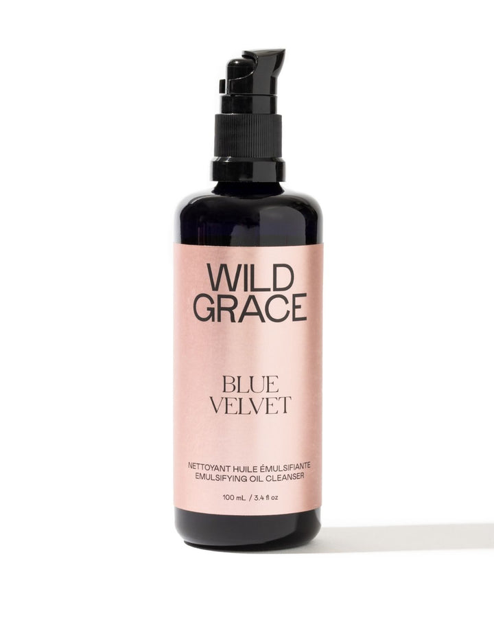 A 100 mL pump bottle of Wild Grace Blue Velvet Emulsifying Oil Cleanser, featuring a black bottle and a metallic pink label, set against a plain white background.