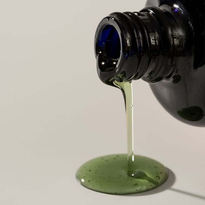 Green liquid being poured from a black bottle onto a white surface.