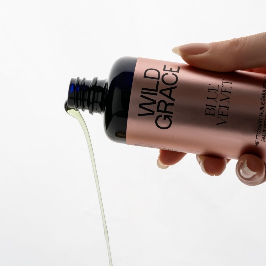 Hand holding a bottle of Wild Grace Blue Velvet nail polish with a light gray background