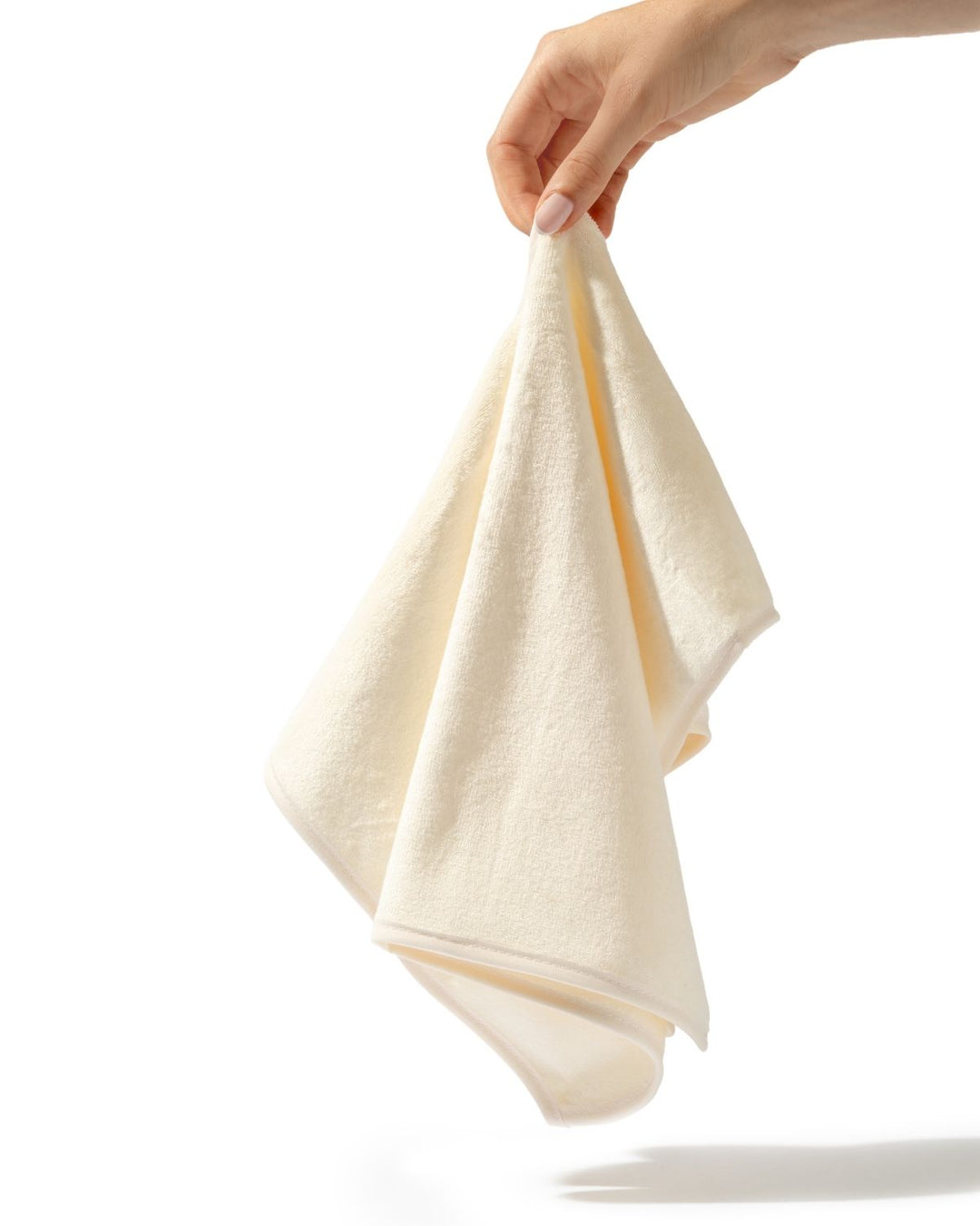 A hand holding a soft, cream-colored cotton towel against a solid white background.