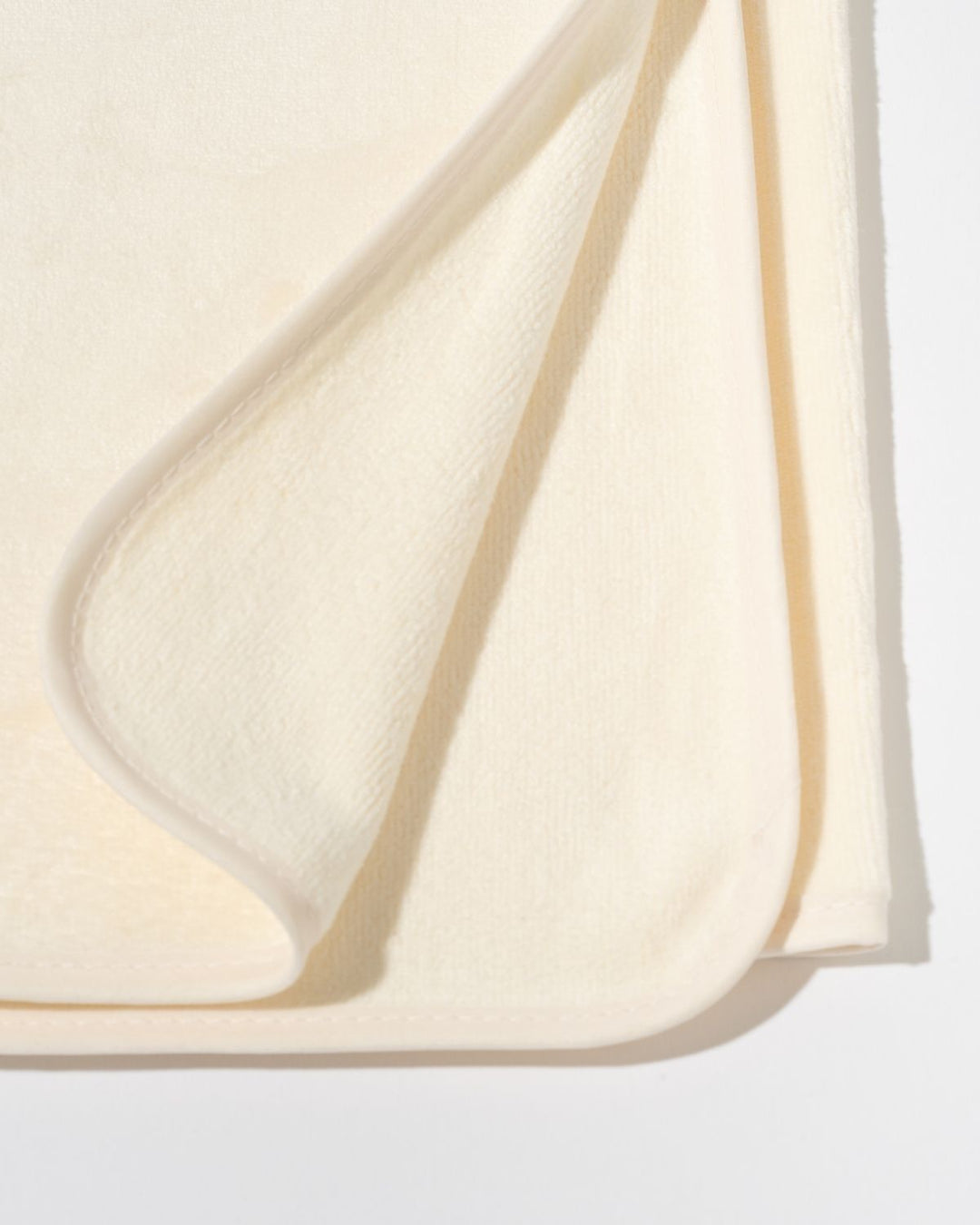 A close-up of a soft cream-colored fabric, likely a baby blanket or towel, folded over to show its plush texture against a clean white background.