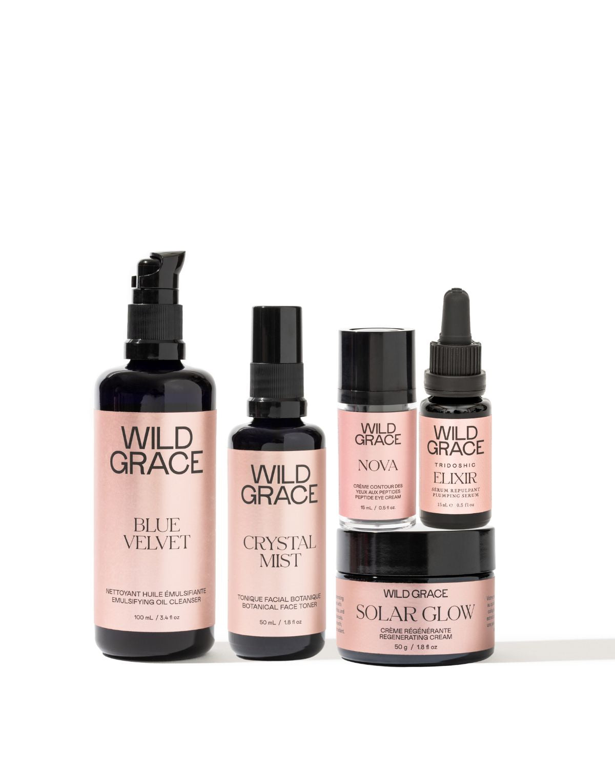 A set of five Wild Grace skincare bottles and jars arranged on a white background, featuring black packaging with soft pink labels. The products include Blue Velvet, Crystal Mist, Nova, Elixir, and Solar Glow.