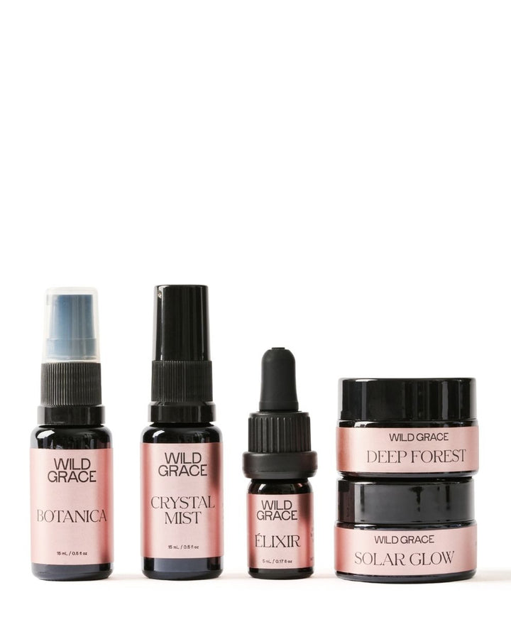 A five-piece Wild Grace skincare set featuring botanical and forest-toned products in dark amber glass bottles and jars with pink labels, arranged on a white background.