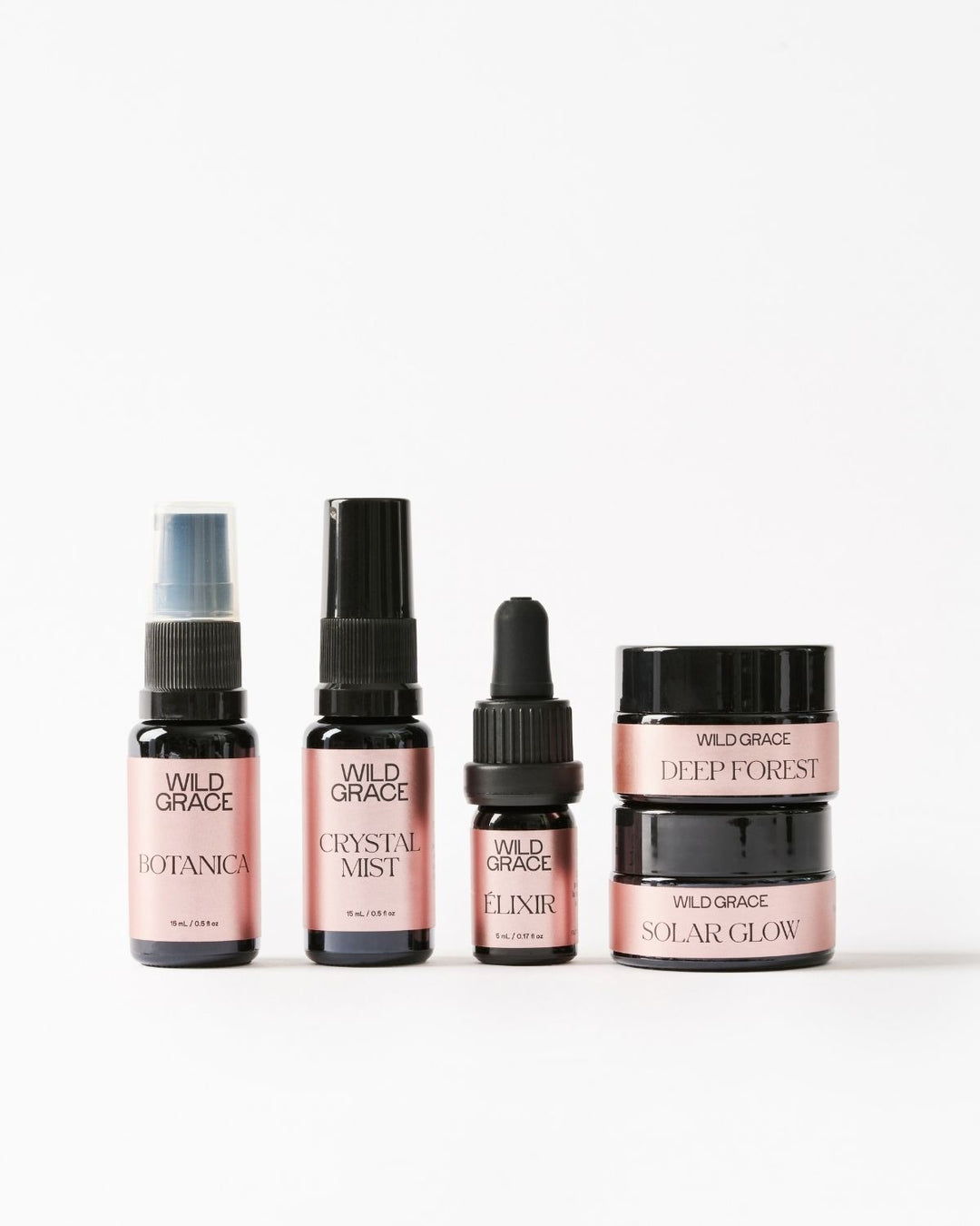 Five Wild Grace skincare bottles and jars arranged on a clean white background, including Botanica spray, Crystal Mist, Elixir dropper, and Deep Forest and Solar Glow jars.