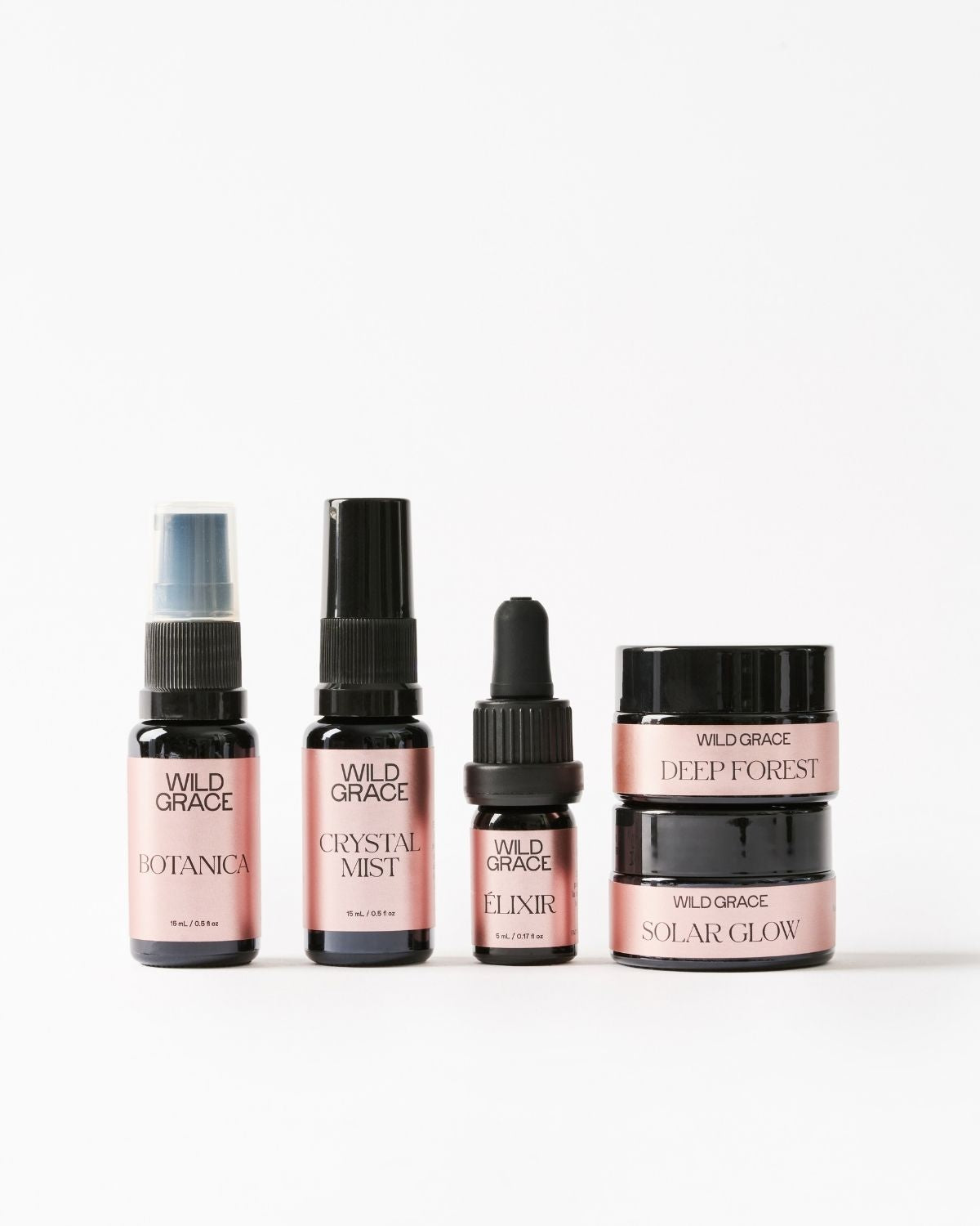 Five Wild Grace skincare bottles and jars arranged on a clean white background, including Botanica spray, Crystal Mist, Elixir dropper, and Deep Forest and Solar Glow jars.