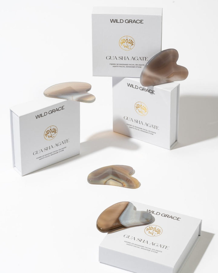 Wild Grace Gua Sha massage stones in various natural stone colors, displayed alongside their white branded packaging boxes on a clean white background.