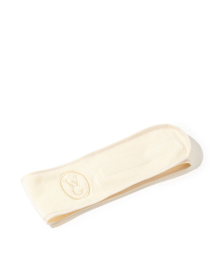 A cream-colored cotton headband with a debossed circular logo, photographed on a clean white background.