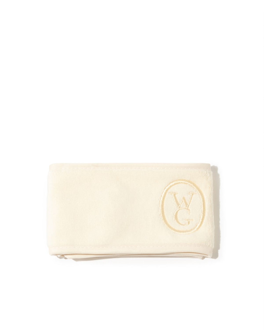 A folded cream-colored cotton towel with a gold embroidered oval logo featuring the letters &