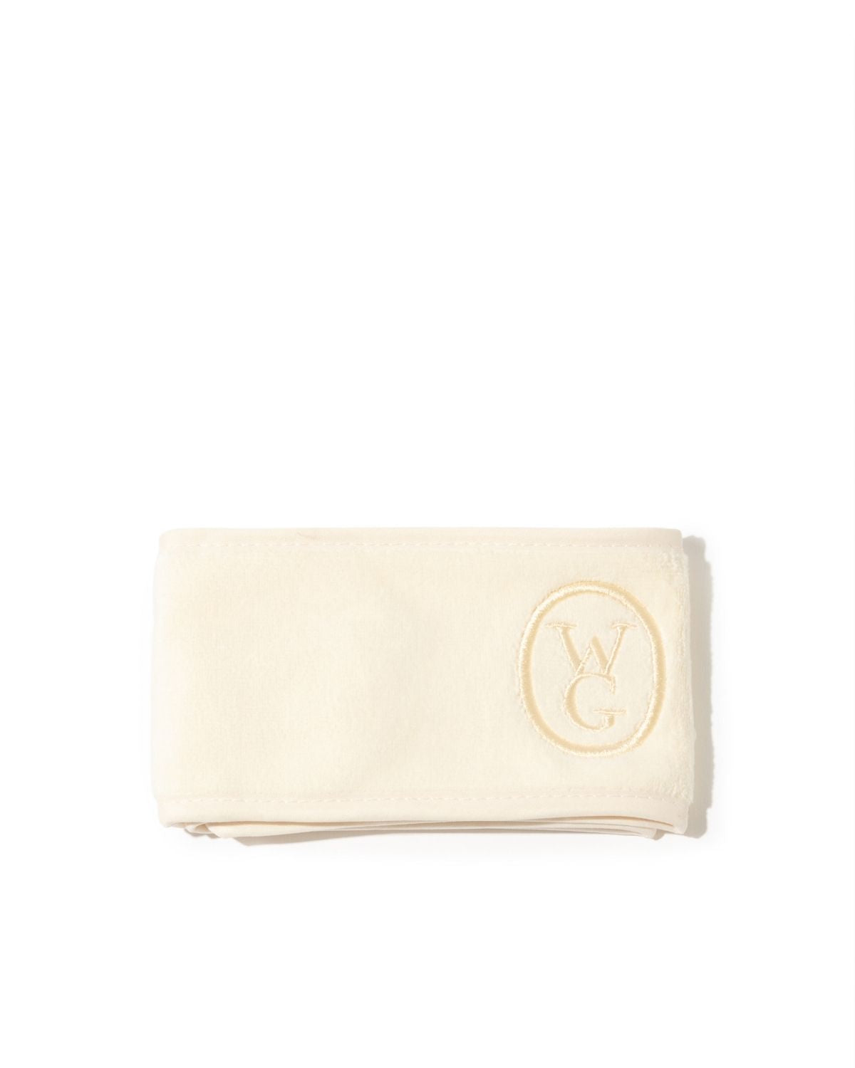 A folded cream-colored cotton towel with a gold embroidered oval logo featuring the letters 'W' and 'G', set against a plain white background.