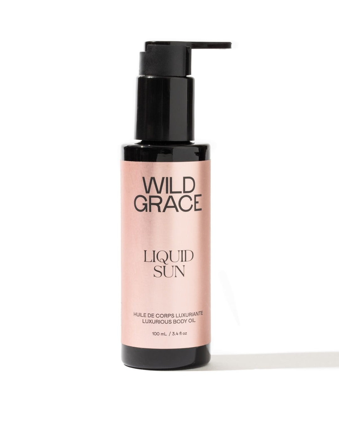 A bottle of Wild Grace Liquid Sun Luxurious Body Oil on a white background. The bottle is black with a black pump dispenser and features a light pink label with black text.