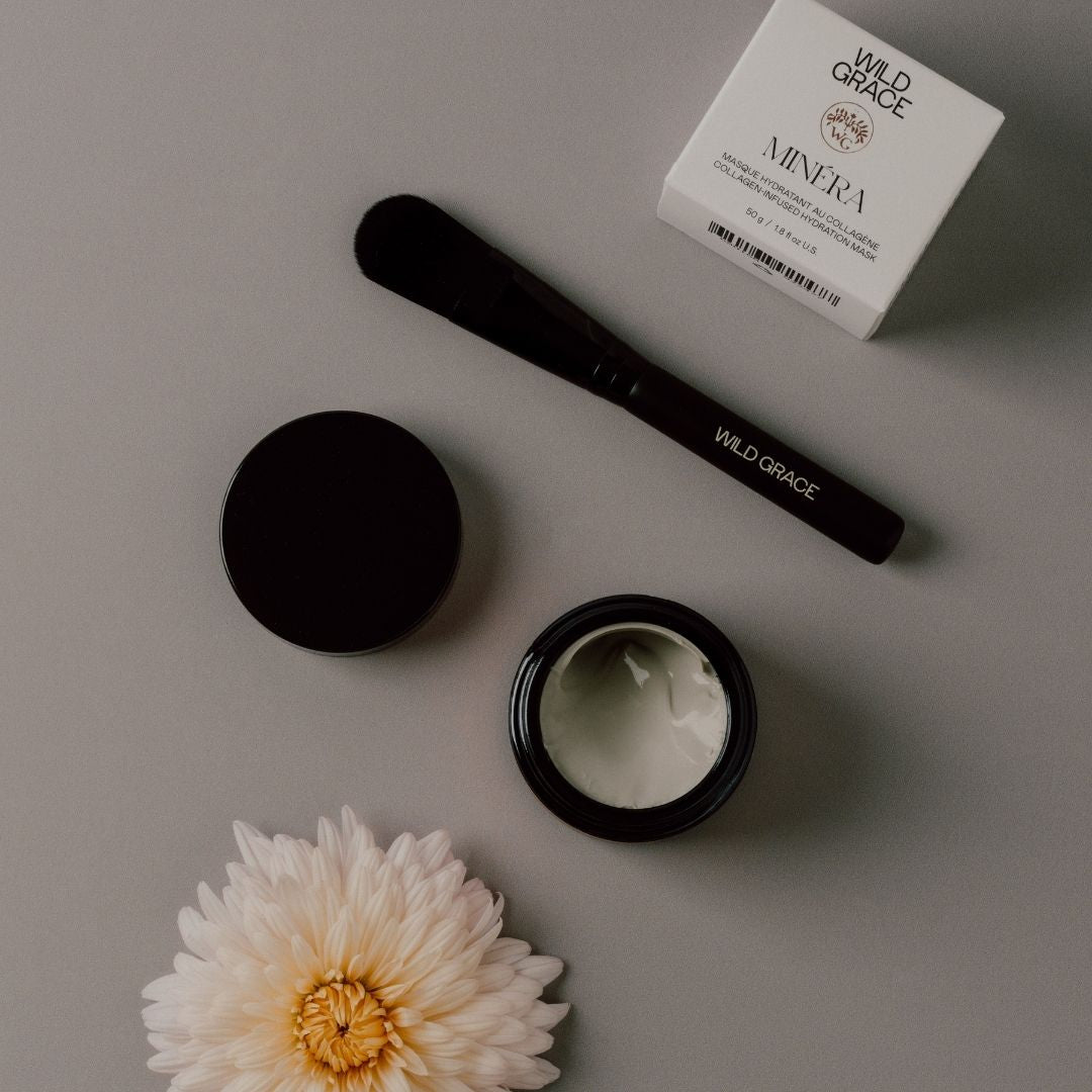 Cosmetic MINÉRA mask by WILD GRACE, including a jar, brush, and box labeled 'Wild Grace' on a gray surface with a flower.