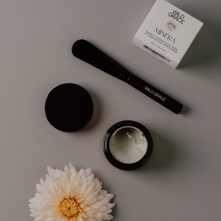 Cosmetic MINÉRA mask by WILD GRACE, including a jar, brush, and box labeled 'Wild Grace' on a gray surface with a flower.
