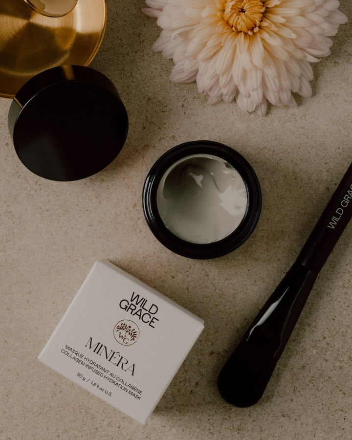 Cosmetic jar of minéra mask by wild grace, box, and brush on a textured surface with a flower.