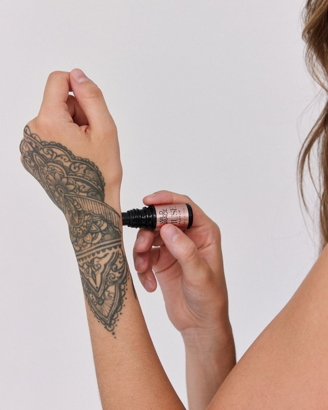 Person applying a rollerball of MUSE essential oil perfume to their tattooed arm against a plain background