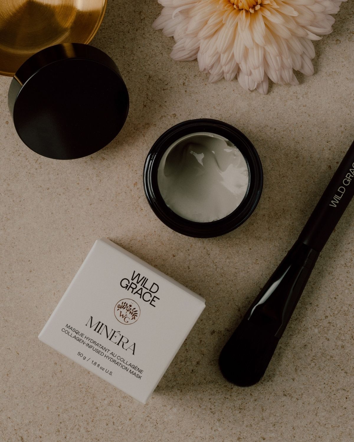 Cosmetic jar, brush, and packaging with 'Wild Grace' branding on a textured surface.