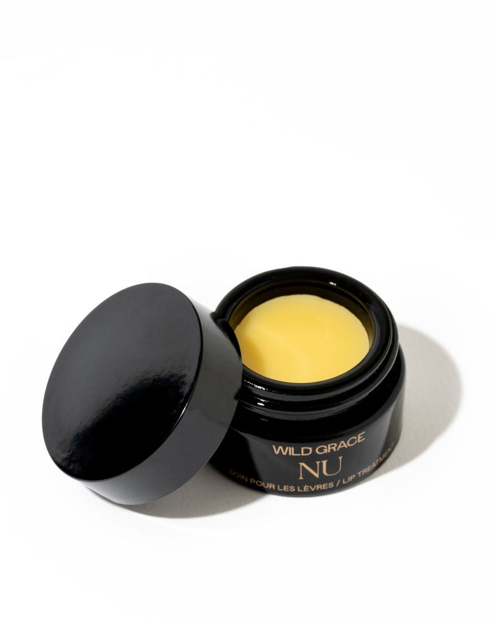 An open black cosmetic jar showing a pale yellow balm or cream, with the lid leaning against it on a clean white background. The jar is labeled &