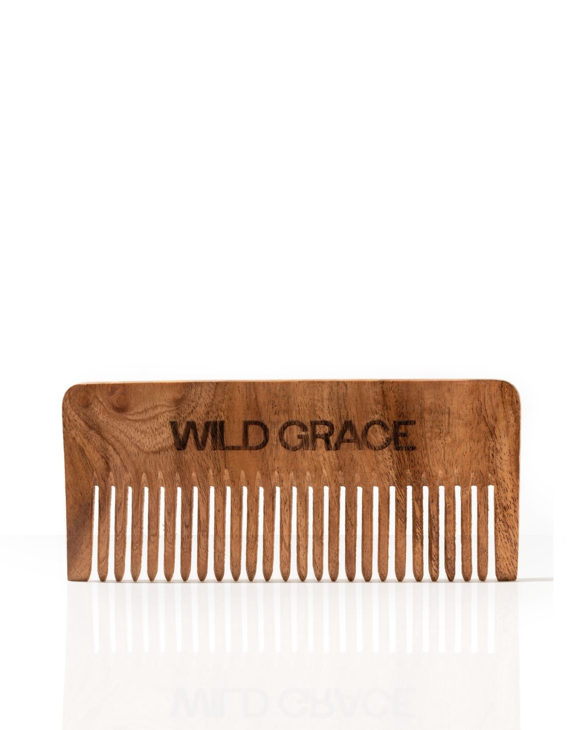 A wooden hair comb with the brand name 'WILD GRACE' engraved on the forehead, shown against a plain white background with a soft reflection below.