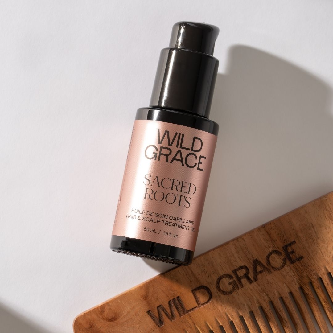 Wild Grace Sacred Roots hair oil bottle with a wooden comb on a light background