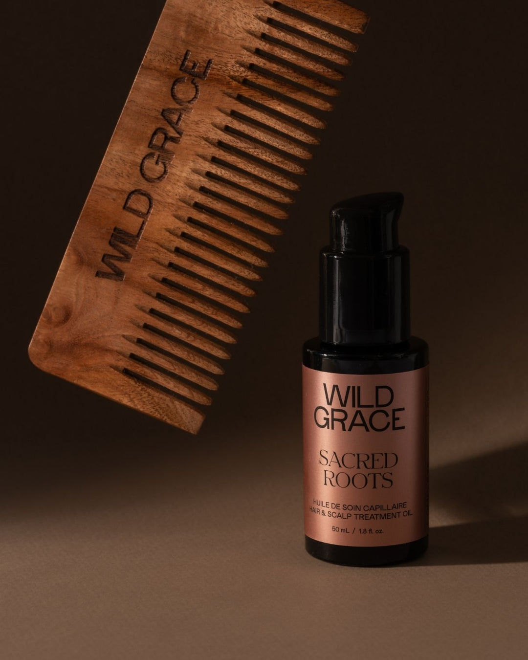 Wooden comb and bottle of Wild Grace Sacred Roots oil on a brown background