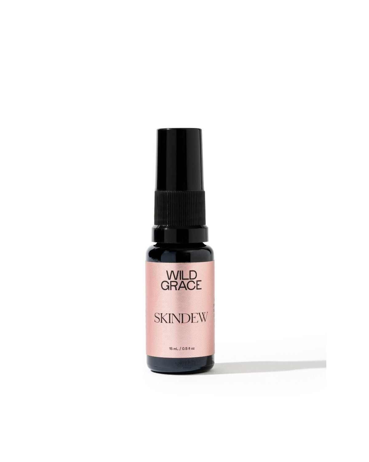 A small amber glass spray bottle with a black spray top and a pale pink label reading 'WILD GRACE SKINDEW' on a clean white background.