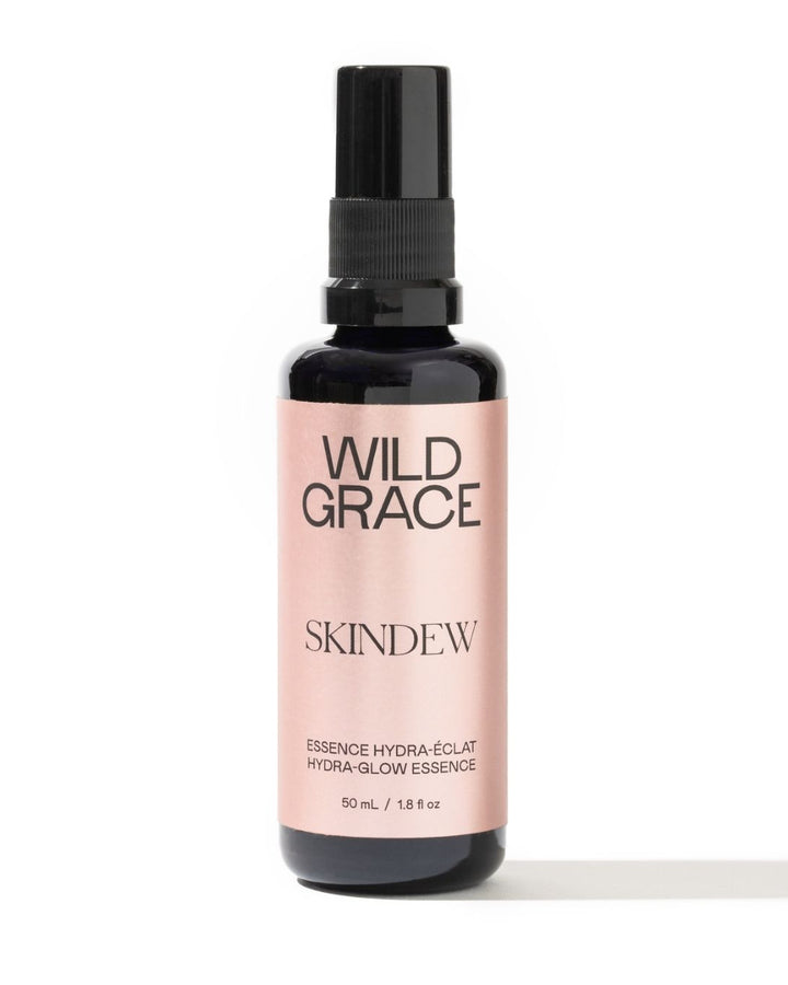 A 50 mL bottle of Wild Grace Skindew Hydra-Glow Essence, featuring a black spray nozzle and a pale pink label on a white background.
