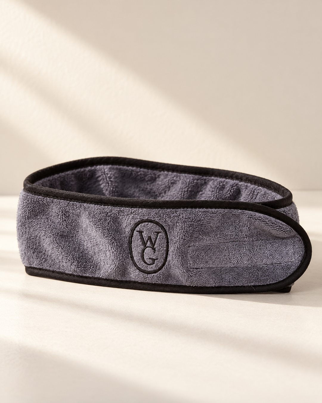 A gray textured microfiber eye mask with black trim and an embroidered circular &