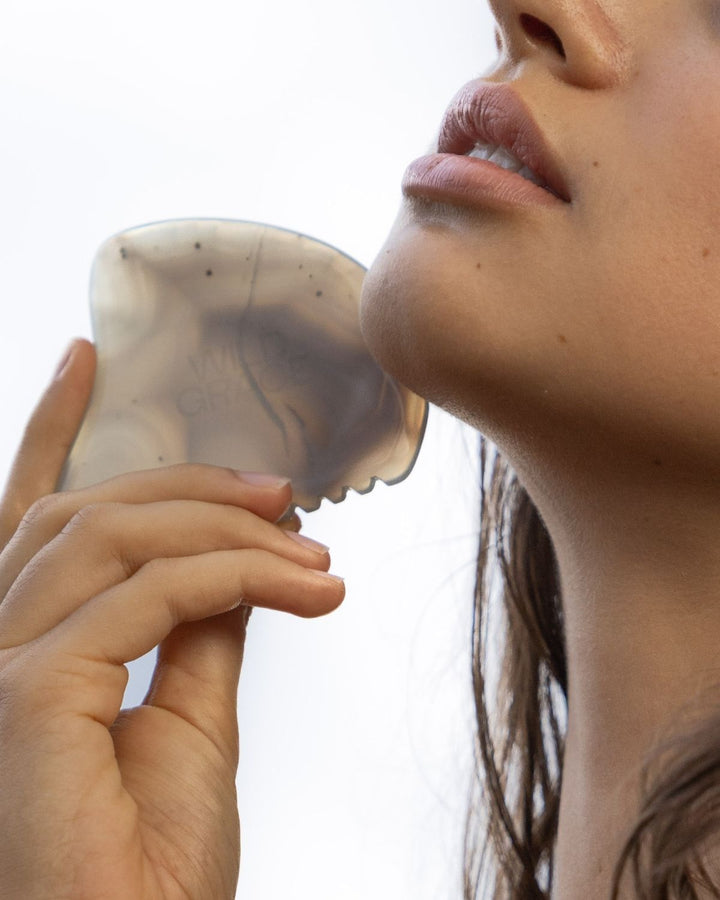 Person using a wild grace gua sha tool on their face with a white background