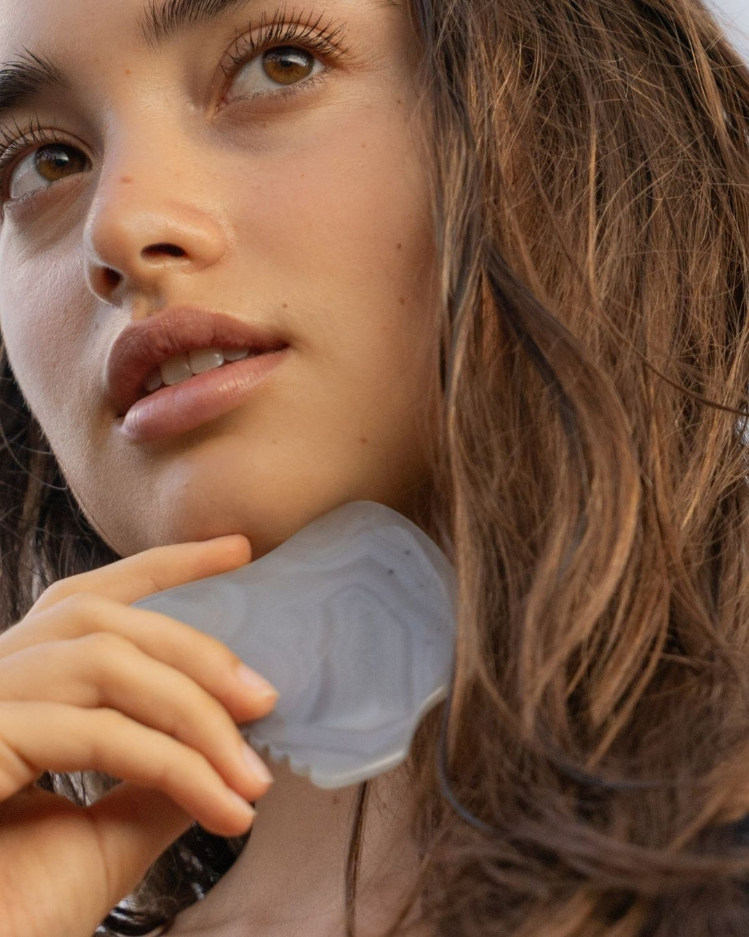 Close-up of a person holding a gray agate gua sha with a blurred background