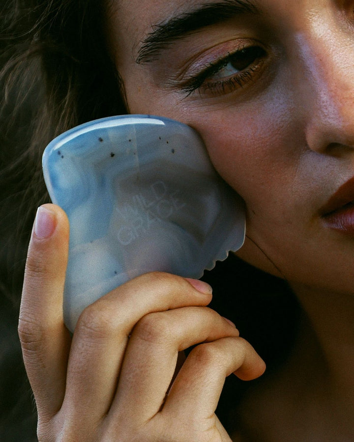 Woman holding a grey agate stone gua sha to their face