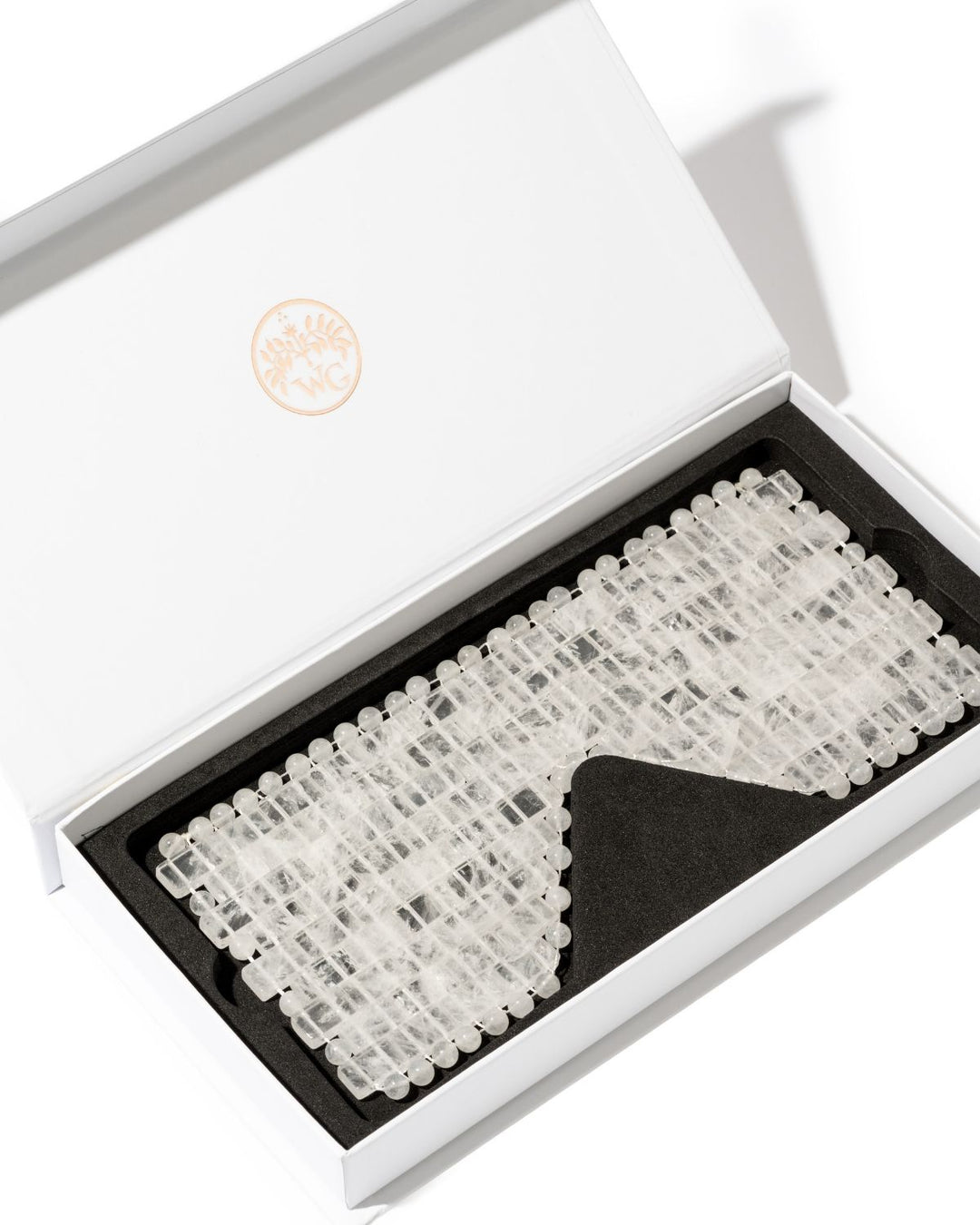 A white presentation box opened to reveal a clear, beaded accessory set on a black insert. The box lid has a subtle circular gold logo, and the product appears to be a set of transparent or translucent decorative beads/charms arranged in rows.