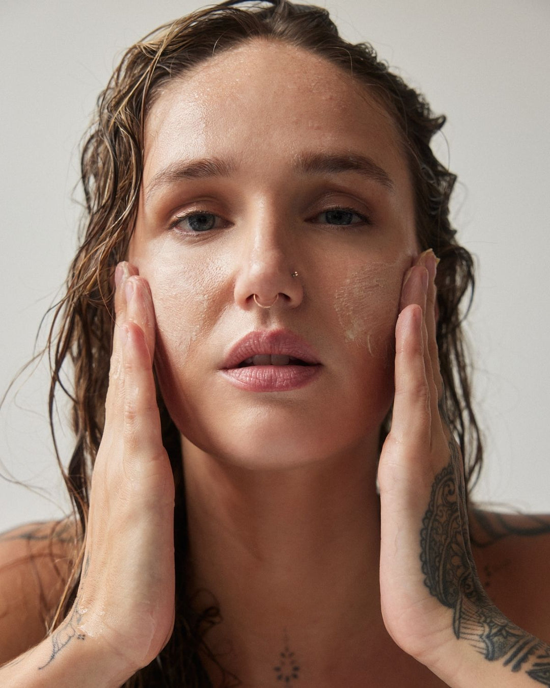 Woman applying the deep forest cleansing balm to her face with a neutral background