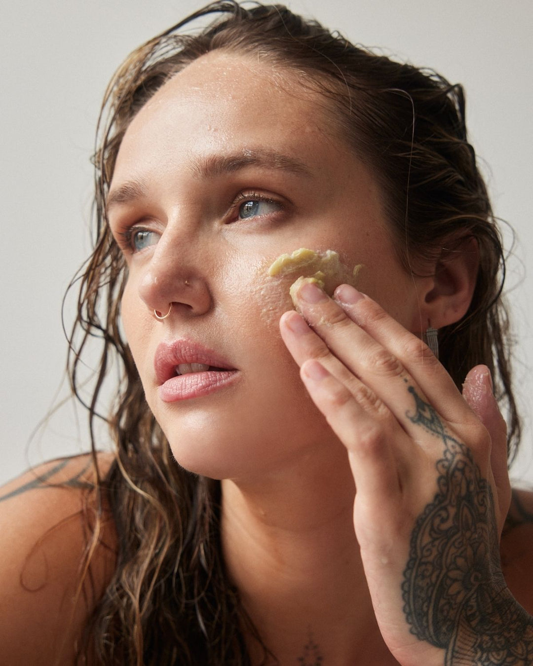 Woman applying a facial product to her cheek with a neutral background