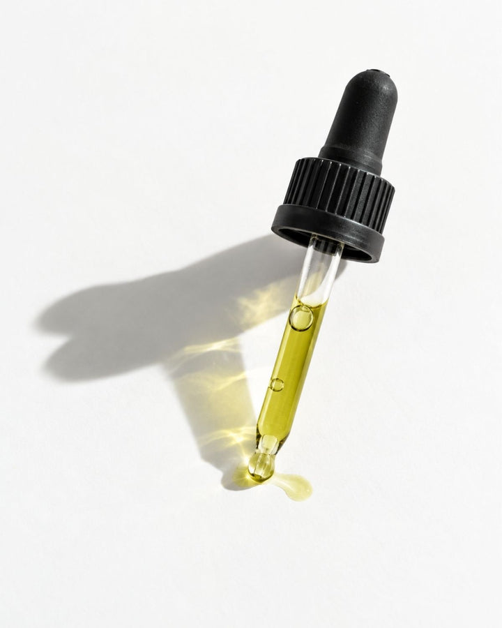 A clear glass dropper bottle filled with yellow-green oil, topped with a black rubber dropper cap, photographed on a white background with a soft shadow.