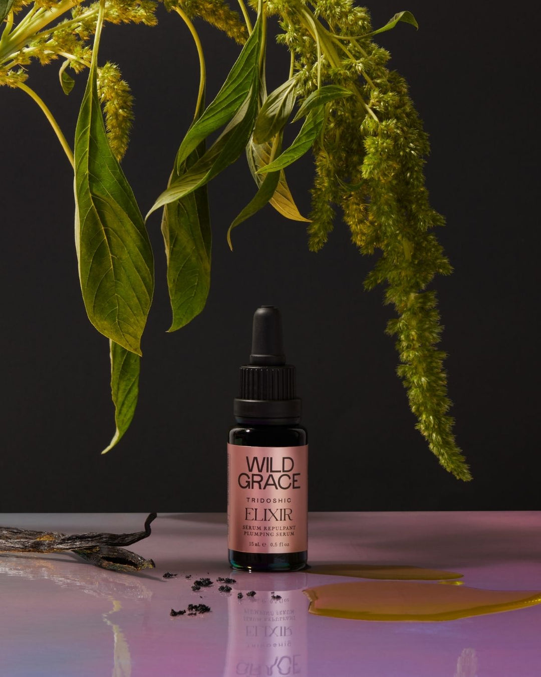 Bottle of Wild Grace Elixir with green leaves on a dark background
