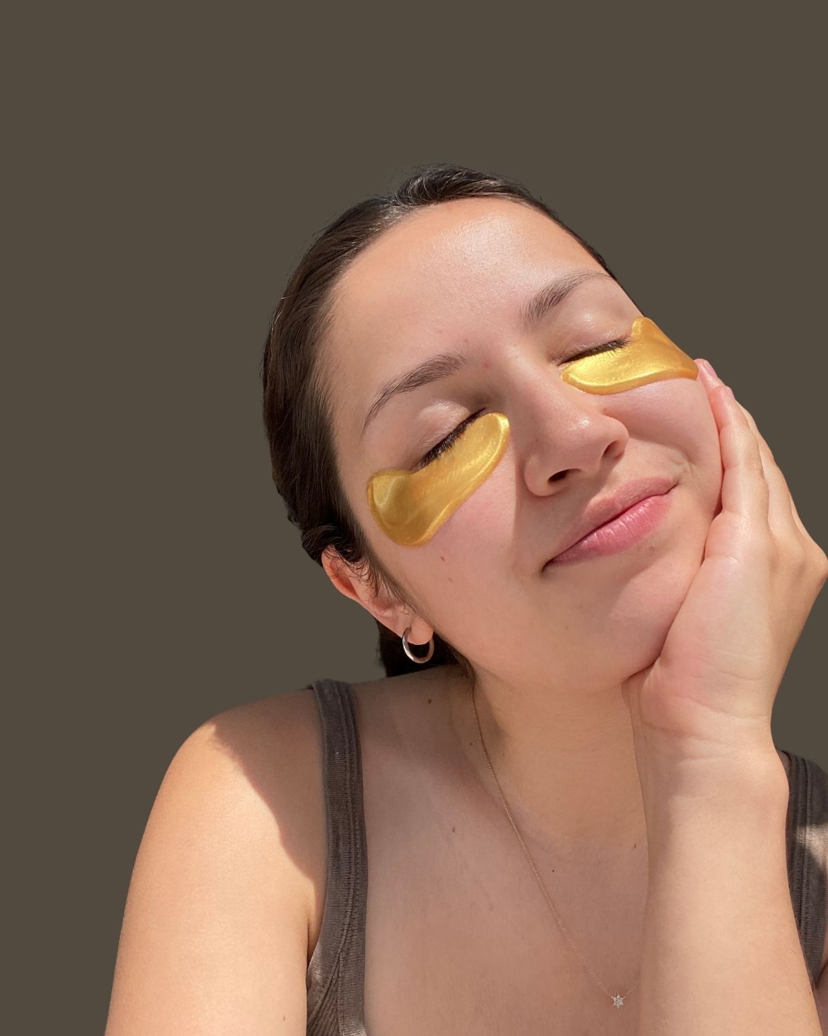 Woman smiling and wearing golden eyes eye masks on a plain background