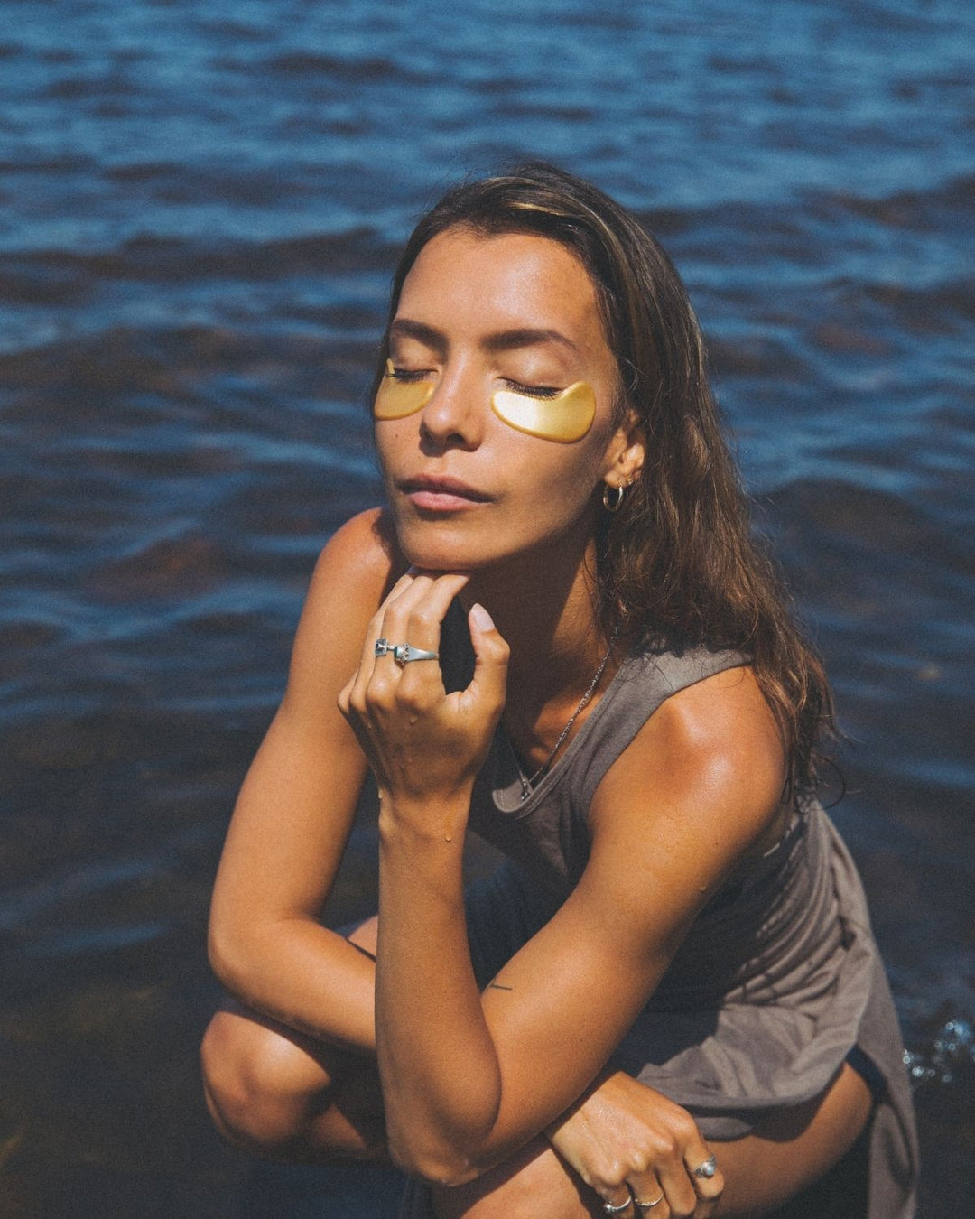 Woman with golden eyes wild grace eye patches sitting by a body of water