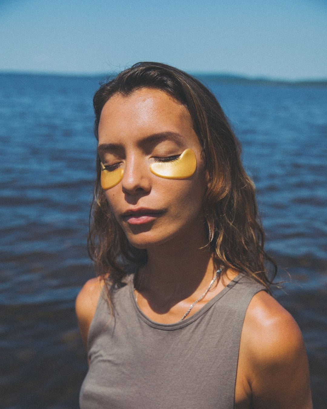 Woman with golden eyes eye patches standing in front of a body of water