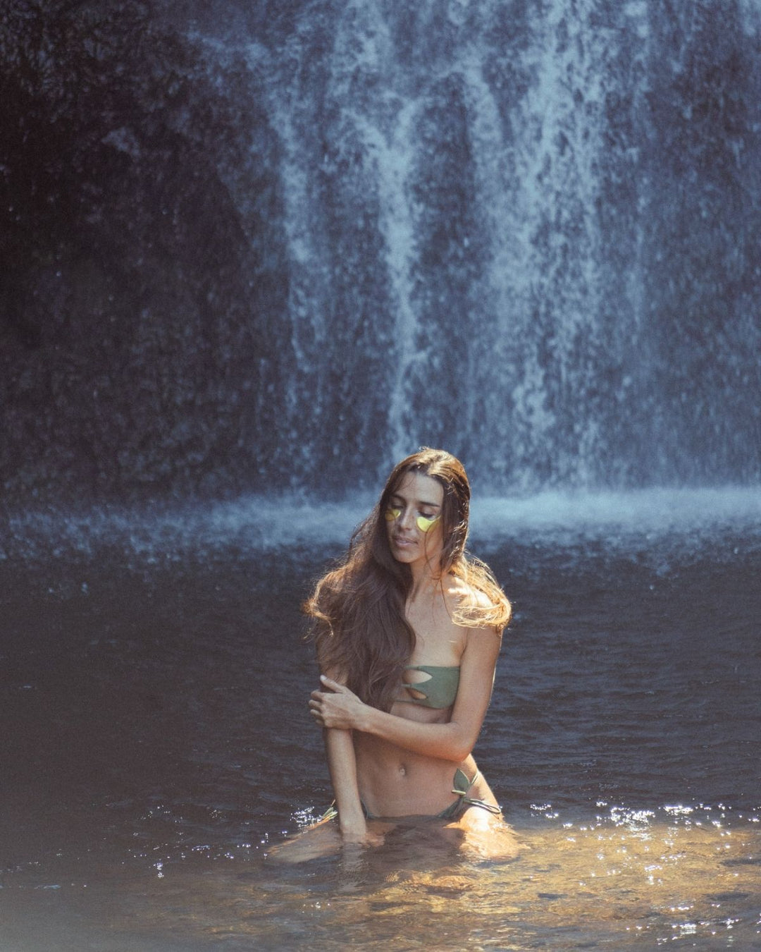 Woman sitting in water with a waterfall in the background