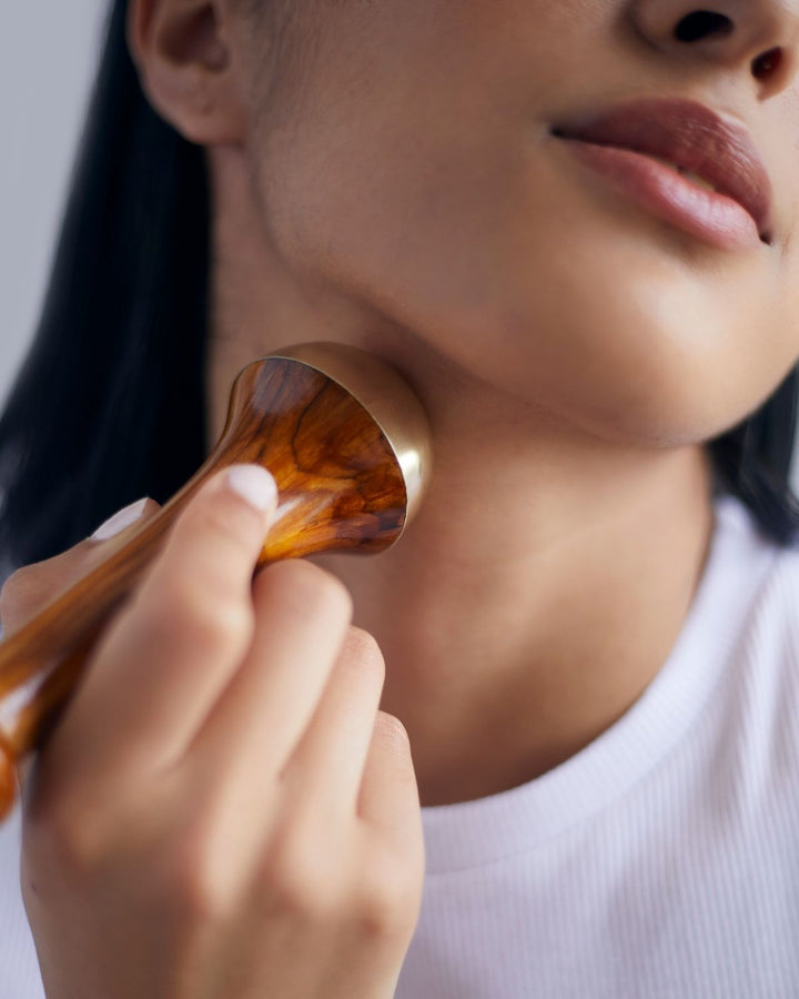 Person holding a kansa wand ool near their neck against a neutral background