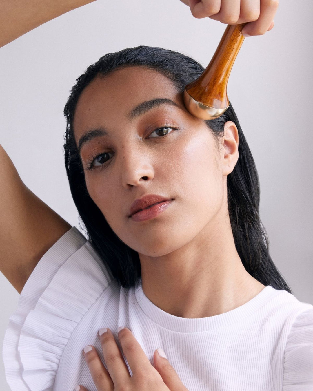 Woman using an ayurvedic kansa wand tool on her hair against a plain background