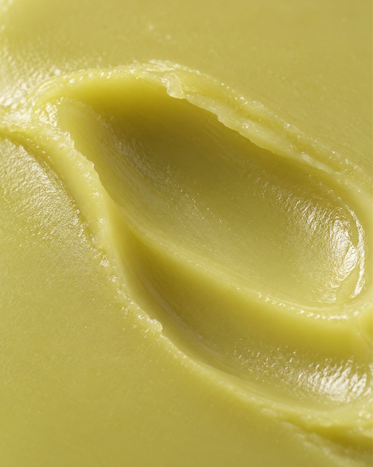 A close-up texture shot of a pale yellow cream or balm with a smooth, swirled surface.