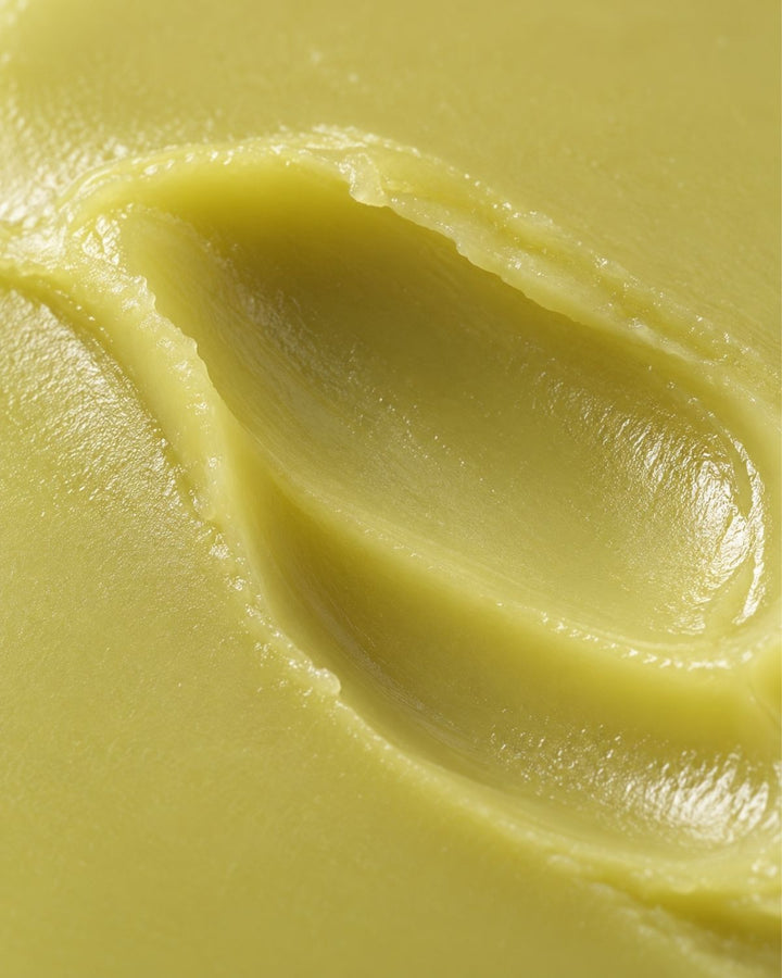 A close-up texture shot of a pale yellow cream or balm with a smooth, swirled surface.